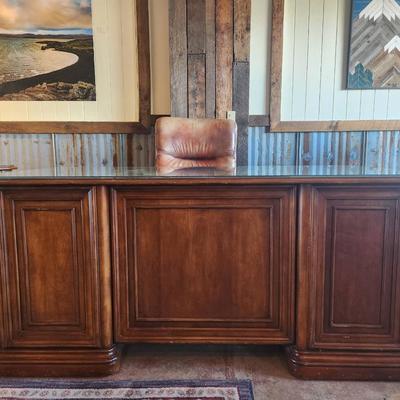 Sale Photo Thumbnail #81: Hooker desk crafted from cherry wood, measuring 6 feet in length, 3 feet in width, and 2.6 feet in height. Features include a glass top for added protection, multiple drawers for storage, and elegant carved details. Labeled with Hooker Furniture branding,