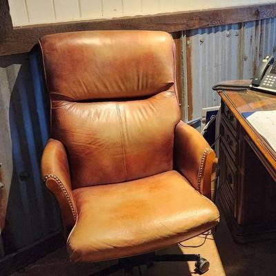 Sale Photo Thumbnail #87: Leather office chair featuring a padded seat, backrest, and armrests. The chair is upholstered in a distressed leather finish with nailhead trim detail. It includes a rolling base with five casters and an adjustable height mechanism for comfort and functi
