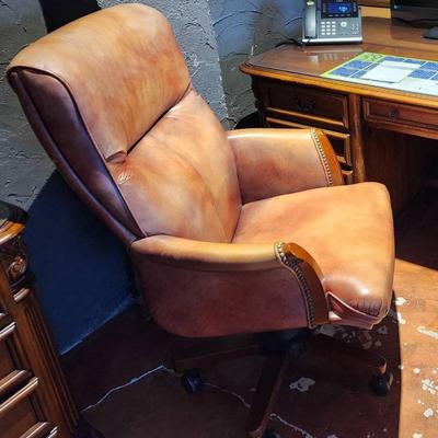 Sale Photo Thumbnail #101: Leather office chair featuring a padded seat, backrest, and armrests. The chair is upholstered in a distressed leather finish with nailhead trim detail. It includes a rolling base with five casters and an adjustable height mechanism for comfort and functi