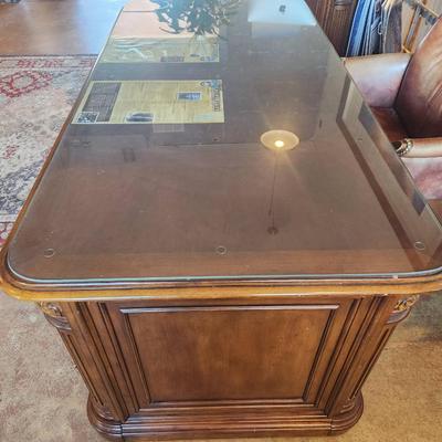 Sale Photo Thumbnail #115: Hooker desk crafted from cherry wood, measuring 6 feet in length, 3 feet in width, and 2.6 feet in height. Features include a glass top for added protection, multiple drawers for storage, and elegant carved details. Labeled with Hooker Furniture branding,