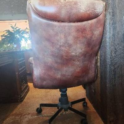 Sale Photo Thumbnail #120: Leather office chair featuring a padded seat, backrest, and armrests. The chair is upholstered in a distressed leather finish with nailhead trim detail. It includes a rolling base with five casters and an adjustable height mechanism for comfort and functi