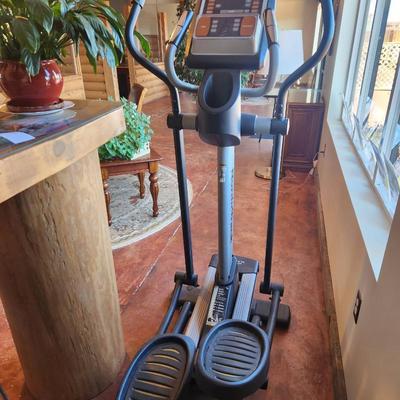 Sale Photo Thumbnail #152: NordicTrack elliptical trainer featuring a built-in display panel for workout tracking. Equipped with foot pedals and upper-body resistance handles. The unit has a sturdy frame and rolling wheels for easy mobility. Appears to be in well-maintained conditi