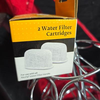 Keurig coffee maker with pod caddy - a red apron - and several Christmas themed mugs.