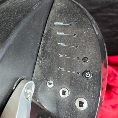 Keurig coffee maker with pod caddy - a red apron - and several Christmas themed mugs.