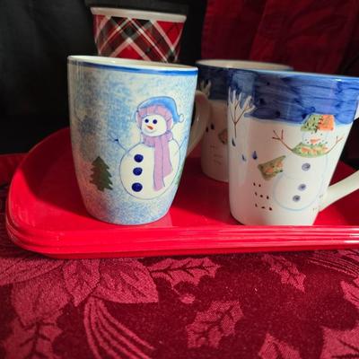 Keurig coffee maker with pod caddy - a red apron - and several Christmas themed mugs.