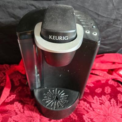 Keurig coffee maker with pod caddy - a red apron - and several Christmas themed mugs.