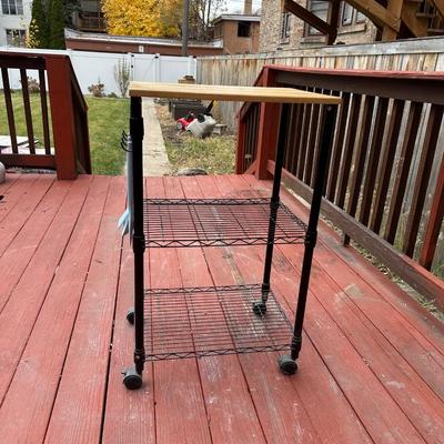 Sale Photo Thumbnail #375: It features two wire shelves and a solid wood (likely maple or butcher block) top for storage and workspace. 
The cart is designed to be functional and efficient, often used in kitchens to keep counters clutter-free. 
It includes four caster wheels which 