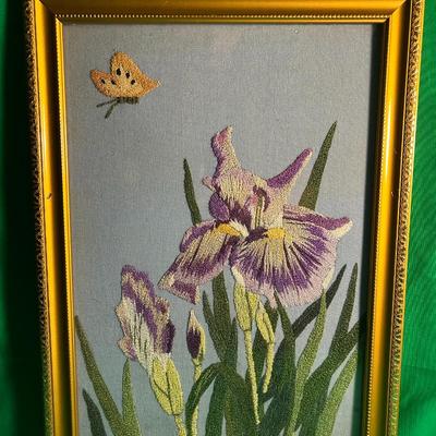 Sale Photo Thumbnail #24: Handcrafted embroidery featuring purple irises and a butterfly, presented in a gold-tone frame with ornate detailing. The artwork uses textured threads to create a detailed and colorful depiction of nature. The frame includes a glass cover to protect the 