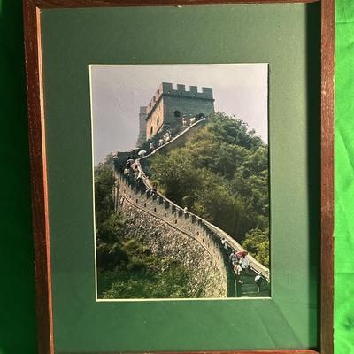 Sale Photo Thumbnail #26: Framed photograph depicting a section of the Great Wall of China. The image features the wall winding through a lush, green hilly landscape with a stone watchtower prominently visible. It is mounted on a green mat and encased in a wooden frame. Frame dime