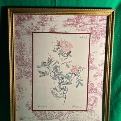 Sale Photo Thumbnail #54: Framed floral artwork featuring a delicate botanical illustration of a flower, accented with soft pinks and greens. The piece has a decorative pink and white patterned matting complementing the artwork. The frame is made of wood with a gold-toned finish a