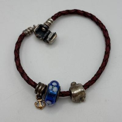 LOT 99; Pandora Leather Braided Bracelet, Blue Glass Floral Charm, Sterling Silver Smiling Budha Charm and a Dangling Anchor Charm