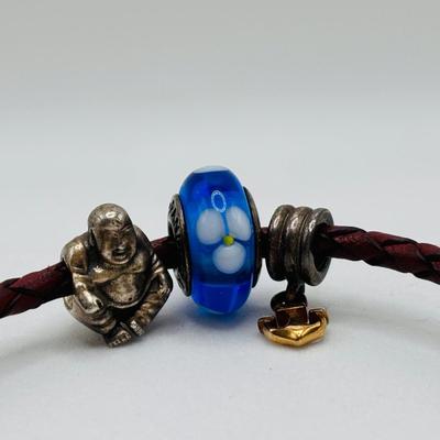 LOT 99; Pandora Leather Braided Bracelet, Blue Glass Floral Charm, Sterling Silver Smiling Budha Charm and a Dangling Anchor Charm
