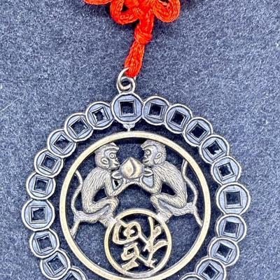 Sale Photo Thumbnail #380: Coin has an image of two monkeys facing each other.  Red cord with 2 tassels at the bottom.  Like new condition.