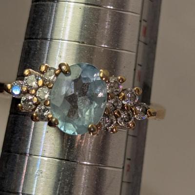 sterling silver ring with oval shaped blue topaz surrounded by small stones, likely CZ