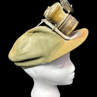 Sale Photo Thumbnail #66: This cap has the original “AutoLite” carbide lamp. The cap and lamp have age related wear. There is no glass lens on the lamp. Not tested. [KD]