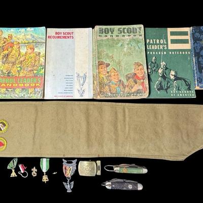 Sale Photo Thumbnail #130: Includes two Boy Scout pocket knives, a belt buckle, three medals, an Eagle Scout award in sterling silver, a merit badge sash, and six books. Total of 14 pieces. [KD]