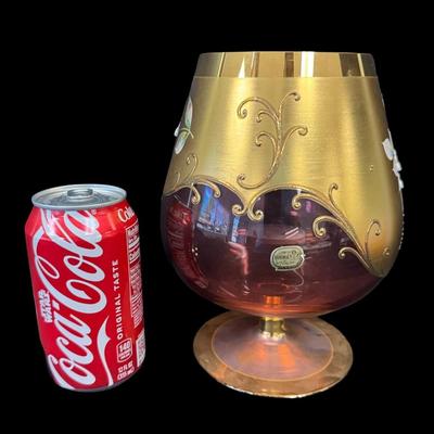 Sale Photo Thumbnail #164: This cranberry glass vase has raised flowers and ornate gold decoration. There is still a paper label affixed. No obvious chips or cracks. Measurement: 8”H x 6” Diameter (at widest point). Pre-auction estimate: $50-$100. [RE]