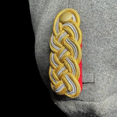 Sale Photo Thumbnail #174: This would have been worn by a General Officer. It is possibly a reproduction or prop. Made from wool, in a field grey color. The red piping on the cuffs aligns with an M36 model greatcoat. Possibly size XL. This has been in a smoky environment, and needs