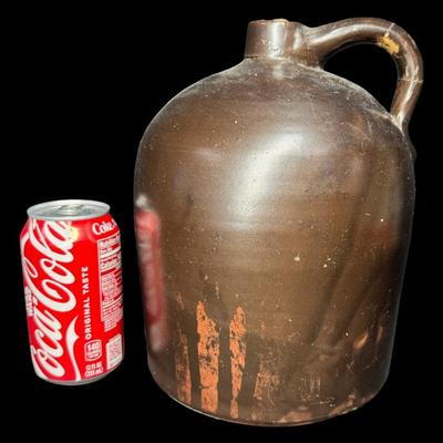 Sale Photo Thumbnail #188: This jug has a deep brown glaze. There is a chip on the base, and the handle has been repaired. There is general age related wear, including some surface scratches. Measurement; 10”H x 7”W. [SR]