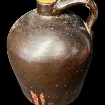 Sale Photo Thumbnail #186: This jug has a deep brown glaze. There is a chip on the base, and the handle has been repaired. There is general age related wear, including some surface scratches. Measurement; 10”H x 7”W. [SR]