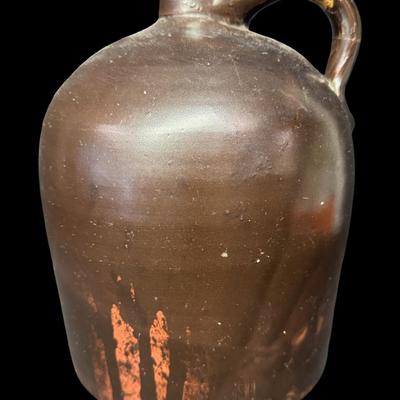 Sale Photo Thumbnail #185: This jug has a deep brown glaze. There is a chip on the base, and the handle has been repaired. There is general age related wear, including some surface scratches. Measurement; 10”H x 7”W. [SR]