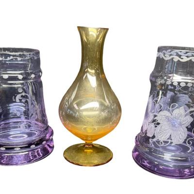 Sale Photo Thumbnail #285: Made in Czechoslovakia. Includes two purple etched beer mugs, and one amber delicate glass vase. Total of three pieces. One of the mugs has a chip on the rim (pictured). Measurement of tallest: 7”H. Pre-auction estimate: $75-$125. [RE]