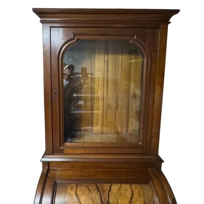 Sale Photo Thumbnail #330: Two piece design featuring a bookcase on top. The lower portion features the cylinder roll. It is most likely made from walnut, with a possible veneer. There is age related wear, including one missing section of moulding on the top right side. Measurement