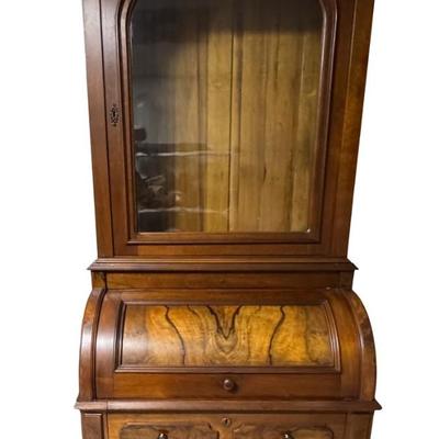 Sale Photo Thumbnail #328: Two piece design featuring a bookcase on top. The lower portion features the cylinder roll. It is most likely made from walnut, with a possible veneer. There is age related wear, including one missing section of moulding on the top right side. Measurement