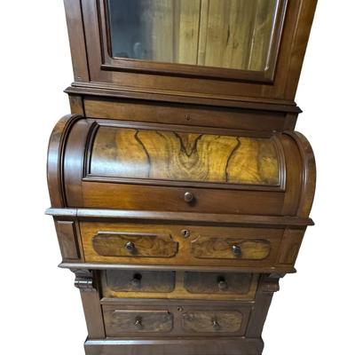 Sale Photo Thumbnail #329: Two piece design featuring a bookcase on top. The lower portion features the cylinder roll. It is most likely made from walnut, with a possible veneer. There is age related wear, including one missing section of moulding on the top right side. Measurement
