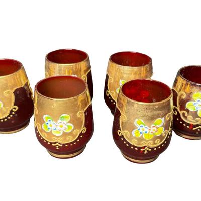 Sale Photo Thumbnail #358: Includes a decanter with a music box in the base, and six cups. It features extensive gold overlay with enamel floral designs. Most likely mid-century. No obvious chips or cracks. The music box appears to be overwound. Measurement of decanter: 13.5”H. [