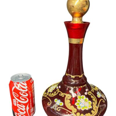 Sale Photo Thumbnail #359: Includes a decanter with a music box in the base, and six cups. It features extensive gold overlay with enamel floral designs. Most likely mid-century. No obvious chips or cracks. The music box appears to be overwound. Measurement of decanter: 13.5”H. [