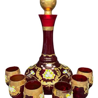 Sale Photo Thumbnail #357: Includes a decanter with a music box in the base, and six cups. It features extensive gold overlay with enamel floral designs. Most likely mid-century. No obvious chips or cracks. The music box appears to be overwound. Measurement of decanter: 13.5”H. [