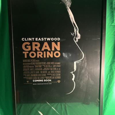 Sale Photo Thumbnail #90: Framed movie poster for the film Gran Torino featuring Clint Eastwood. The poster includes promotional text such as 'Coming Soon' and showcases the title prominently over an artistic profile image of the actor. The poster is enclosed in a black frame and 