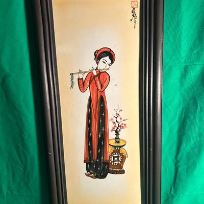Sale Photo Thumbnail #102: Hand-painted artwork on a ceramic tile featuring a Vietnamese woman in traditional attire playing a flute. The piece is set in a black wooden frame with a green backdrop. The intricate details include a decorative pot with flowers. Artist's signature and 