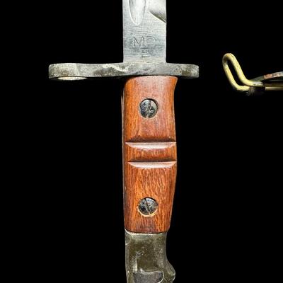 Sale Photo Thumbnail #539: This is an exact reproduction of the classic WW1 Enfield M-1917 bayonet. It has hardwood grips, and comes with a steel-mounted leather scabbard complete with correct hooks. This bayonet was also the standard issue for military shotguns, AKA “Trench Guns