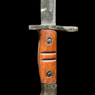 Sale Photo Thumbnail #540: This is an exact reproduction of the classic WW1 Enfield M-1917 bayonet. It has hardwood grips, and comes with a steel-mounted leather scabbard complete with correct hooks. This bayonet was also the standard issue for military shotguns, AKA “Trench Guns