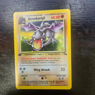 Sale Photo Thumbnail #9: First Edition Aerodactyl Pokemon card from the Fossil series. Features Aerodactyl with 60 HP and the Wing Attack move. The card displays the First Edition stamp on the front. Card is standard size for Pokemon trading cards and includes full artwork design