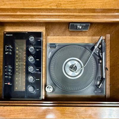 Sale Photo Thumbnail #572: From the early 1970's, pecan finish. Untested. Contains a record player and AM/FM Stereo Receiver Caster wheels underneath to make repositioning easy. Measures approx. 54" x 20" x 27" high. Speakers measure 16" x 11" x 23" high. Includes original paperwor
