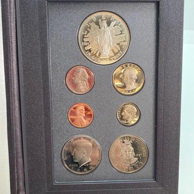 LOT 105: United States Mint 1989 Prestige Set with 1989 Congressional Silver Dollar and Half Dollar in Presentation Book with Certificate...