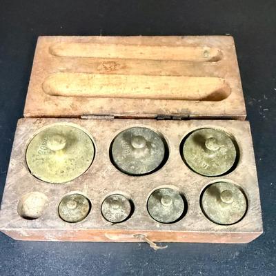 Sale Photo Thumbnail #665: Antique set of brass scale weights in a wooden box. 7 weights are included, the smallest one is missing.  Box hinge is broken.