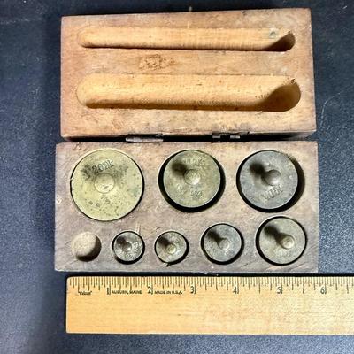 Sale Photo Thumbnail #670: Antique set of brass scale weights in a wooden box. 7 weights are included, the smallest one is missing.  Box hinge is broken.
