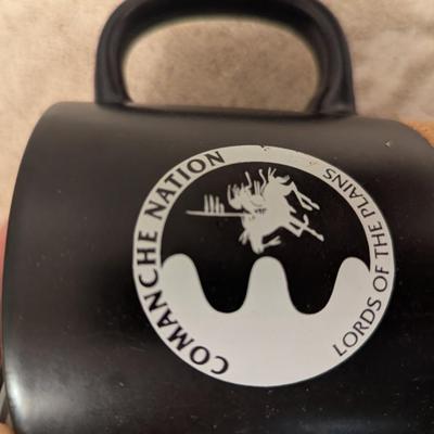 black ceramic mug with a cork base and lid, featuring the Comanche Nation "Lords of the Plains" logo