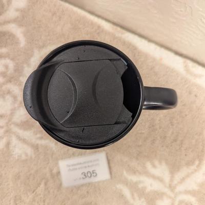 black ceramic mug with a cork base and lid, featuring the Comanche Nation "Lords of the Plains" logo