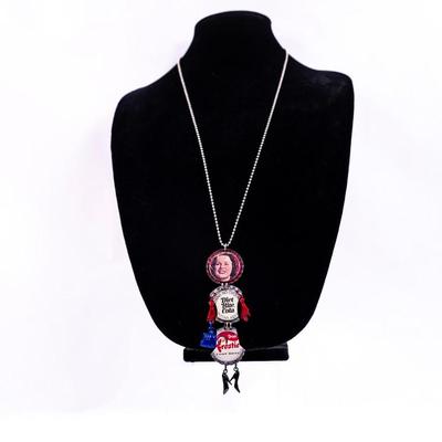 Sale Photo Thumbnail #420: This is a handmade novelty necklace made from vintage Pabt Blue Ribbon and Frostie Root Beer bottle caps. Its features a figural design resembling a person, with the bottle caps forming the body and painted metal pieces for the limbs.