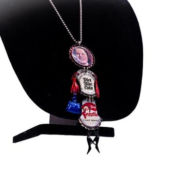 Sale Photo Thumbnail #424: This is a handmade novelty necklace made from vintage Pabt Blue Ribbon and Frostie Root Beer bottle caps. Its features a figural design resembling a person, with the bottle caps forming the body and painted metal pieces for the limbs.