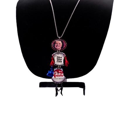 Sale Photo Thumbnail #421: This is a handmade novelty necklace made from vintage Pabt Blue Ribbon and Frostie Root Beer bottle caps. Its features a figural design resembling a person, with the bottle caps forming the body and painted metal pieces for the limbs.