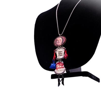 Sale Photo Thumbnail #423: This is a handmade novelty necklace made from vintage Pabt Blue Ribbon and Frostie Root Beer bottle caps. Its features a figural design resembling a person, with the bottle caps forming the body and painted metal pieces for the limbs.
