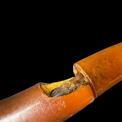 Sale Photo Thumbnail #227: Two pieces. Each is hand carved. One is unused. The amber colored piece has a crack (pictured), and may have been previously used. Two pipe stands are also included. Measurement of longest pipe: 5.75”L. [JP]