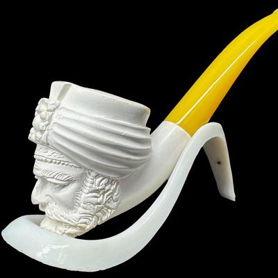 Sale Photo Thumbnail #224: Two pieces. Each is hand carved. One is unused. The amber colored piece has a crack (pictured), and may have been previously used. Two pipe stands are also included. Measurement of longest pipe: 5.75”L. [JP]