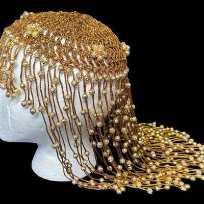 Sale Photo Thumbnail #292: This piece is in the style of a 1920s Flapper headdress. It is gold in color, and features beads throughout. The skull cap is woven. The beaded fringe is intact. Measurement: 16”L. [JP]